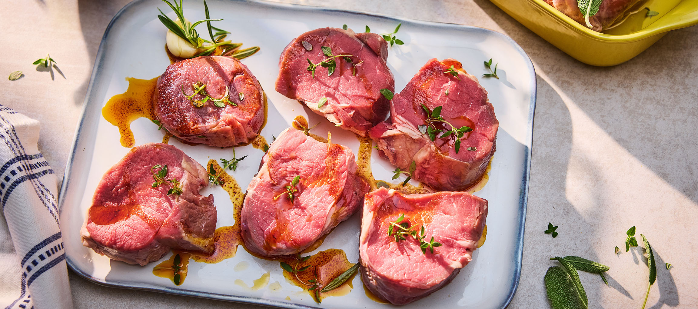 Frische Rindersteaks mit Kräutern und Öl auf einer weißen Platte.