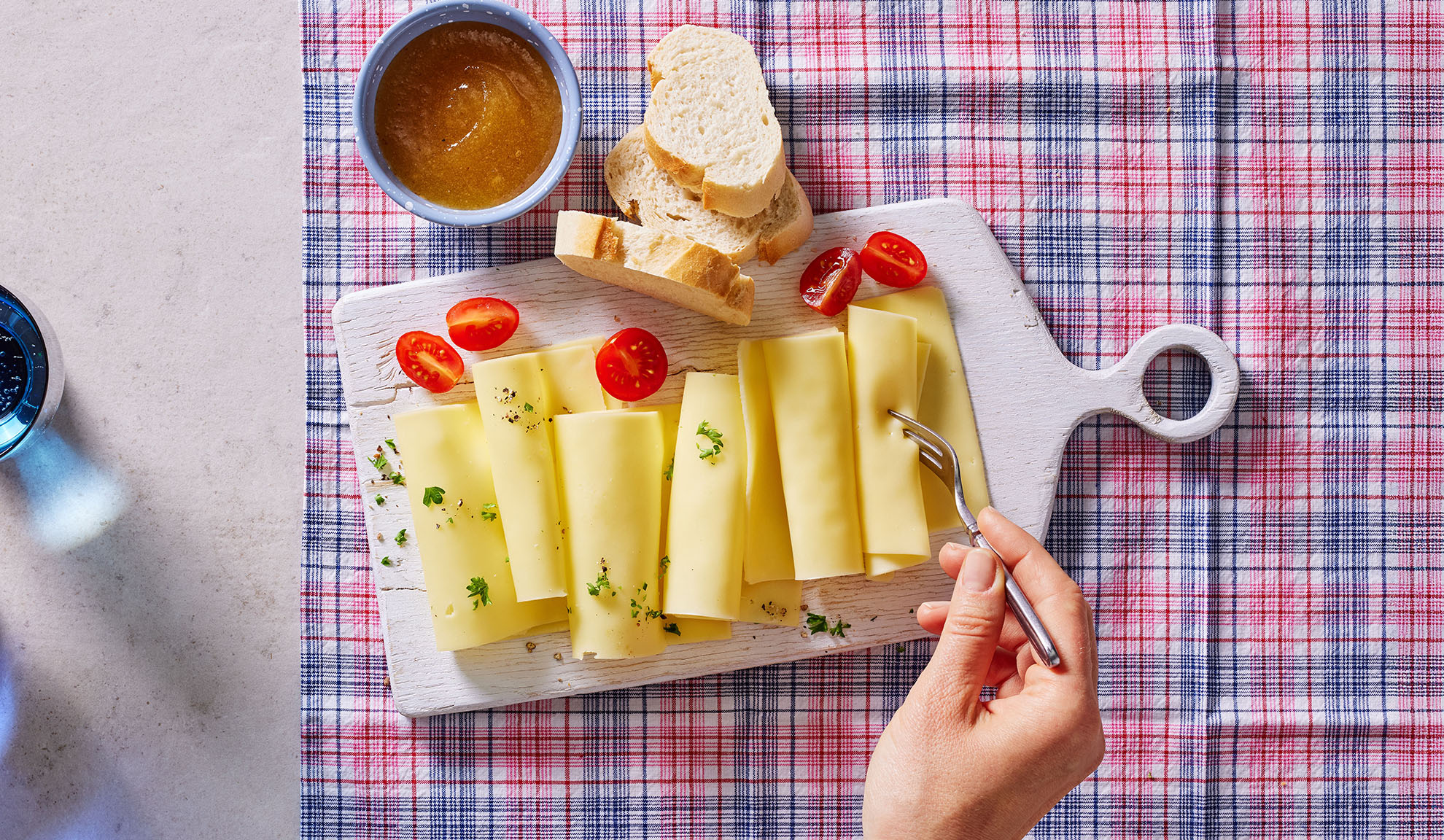 Käsescheiben, Kirschtomaten, Brot und Marmelade auf einem Servierbrett.