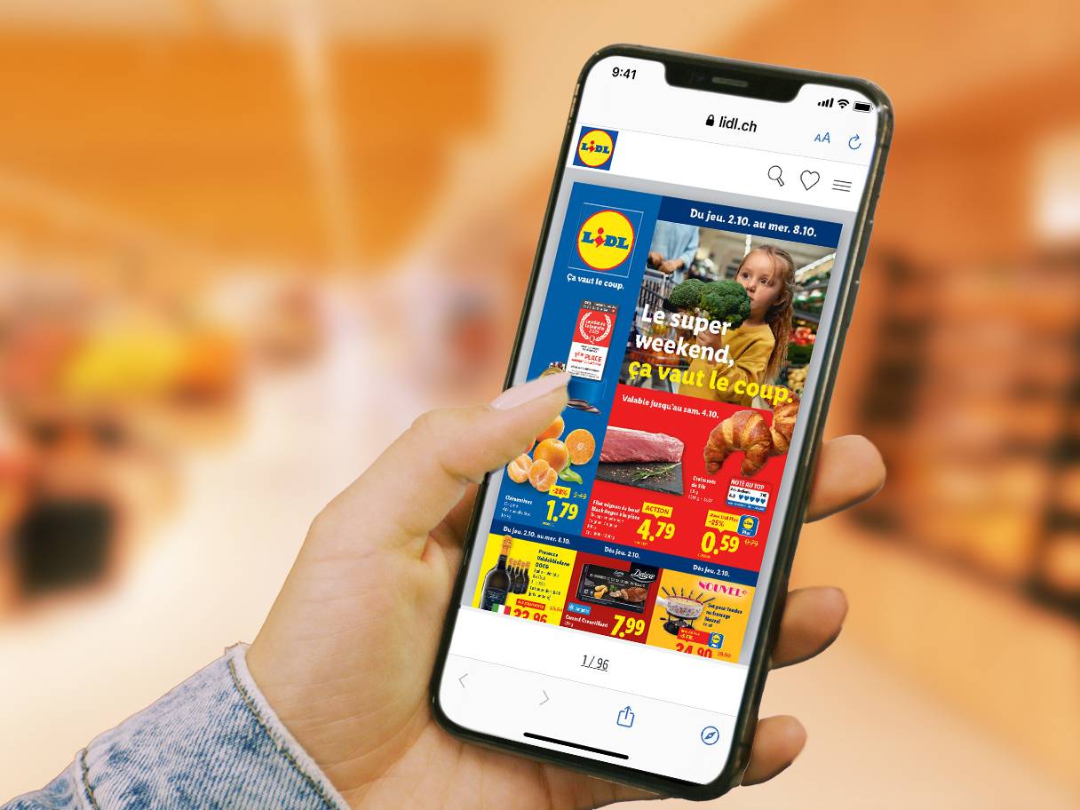 Une personne tient un smartphone affichant une publicité Lidl pour des oranges, de la viande et des croissants.