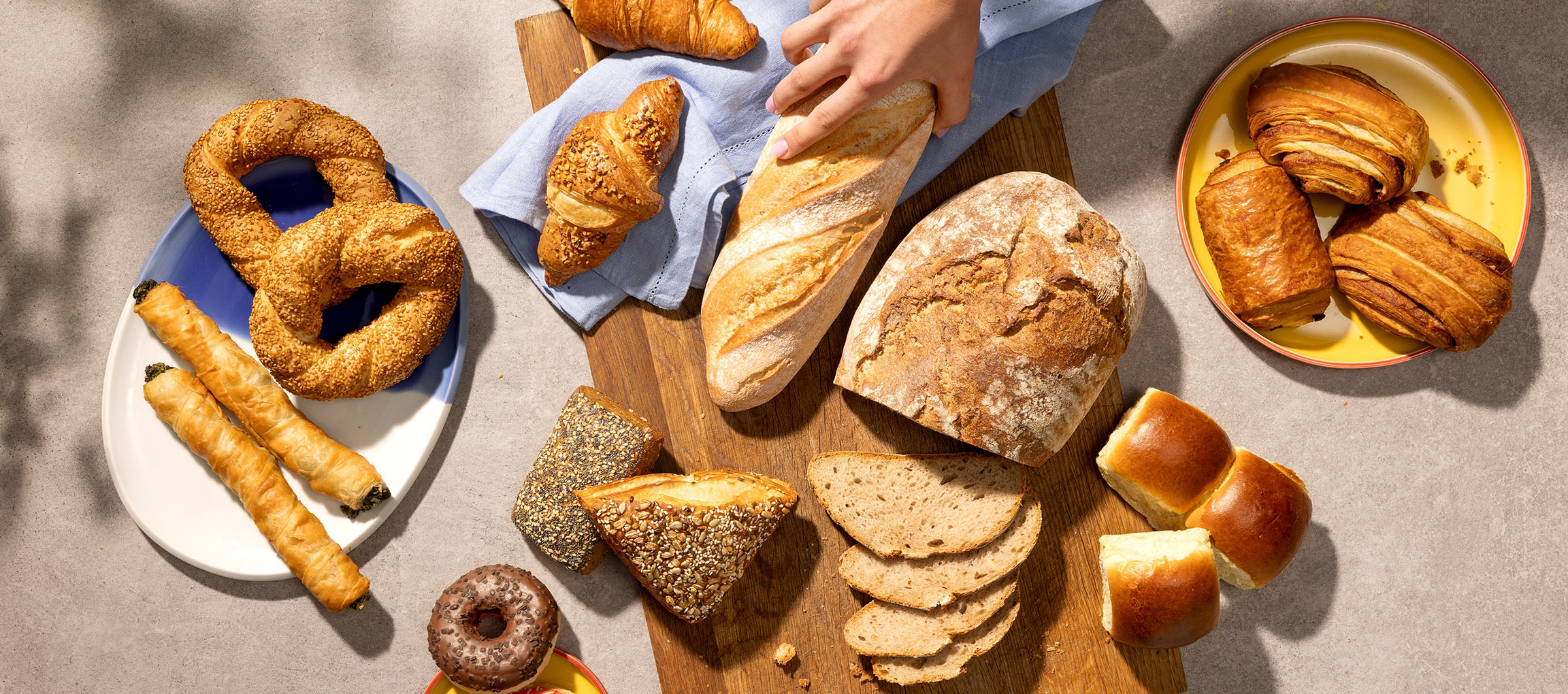 Assortimento di prodotti da forno e pane, inclusi pretzel, croissant e baguette, su un tavolo.
