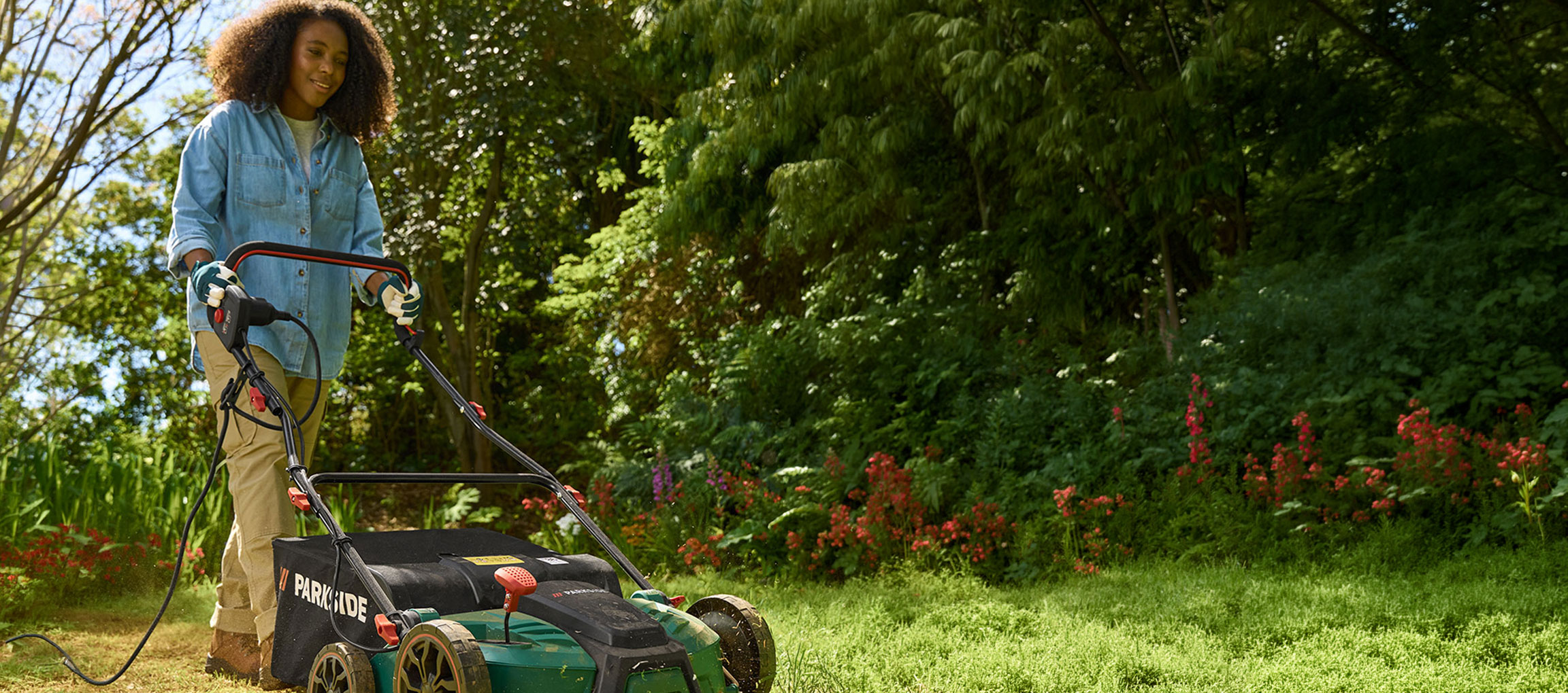 Frau in einem Garten benutzt einen elektrischen Rasenmäher zum Rasenmähen.