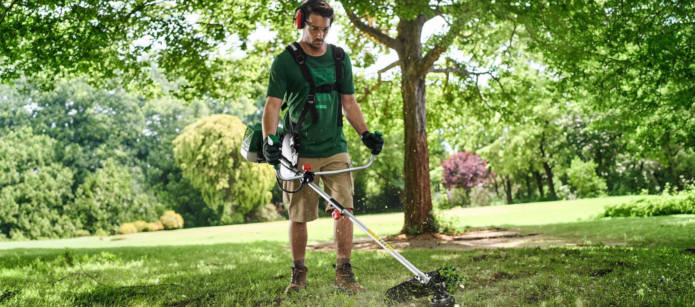Homme avec une débroussailleuse et un équipement de protection tondant l'herbe dans un jardin.