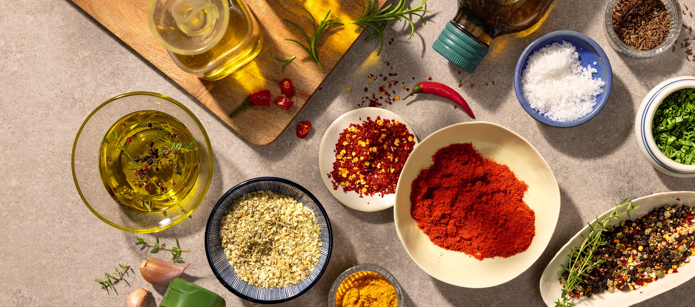 Olio d'oliva, spezie e peperoncini su un tagliere di legno e un tavolo di pietra.