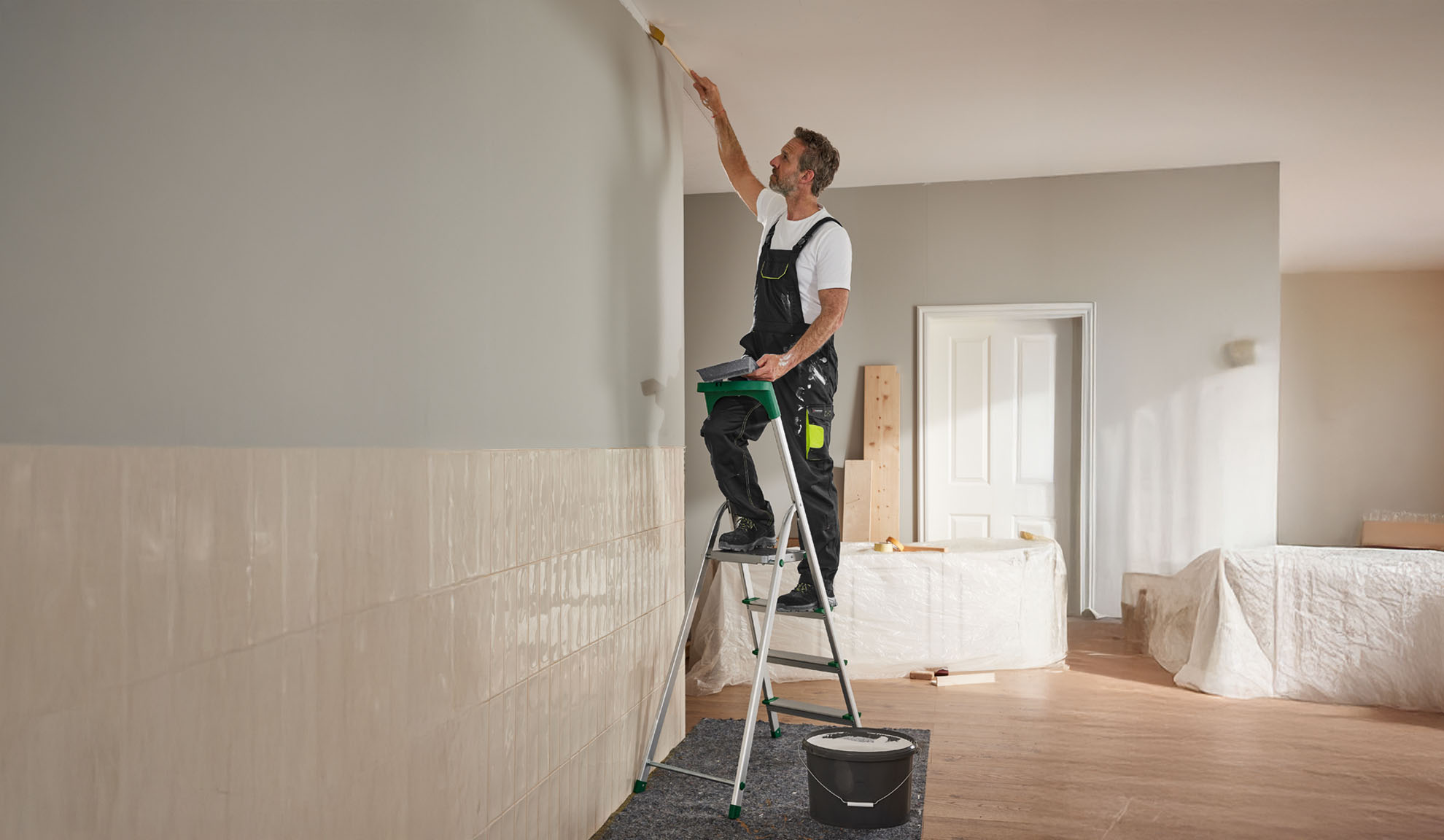 Ein Mann streicht mit einem Pinsel und einer Trittleiter eine Wand.
