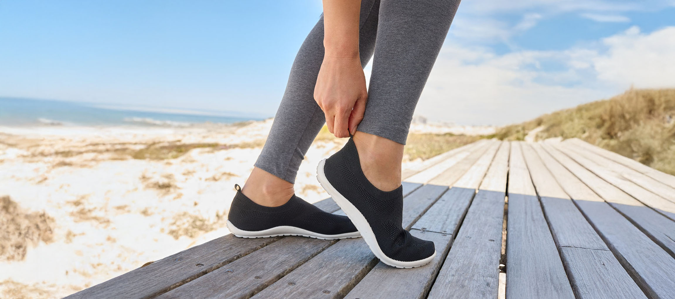 Frau zieht sich schwarze Sportschuhe am Strand an.