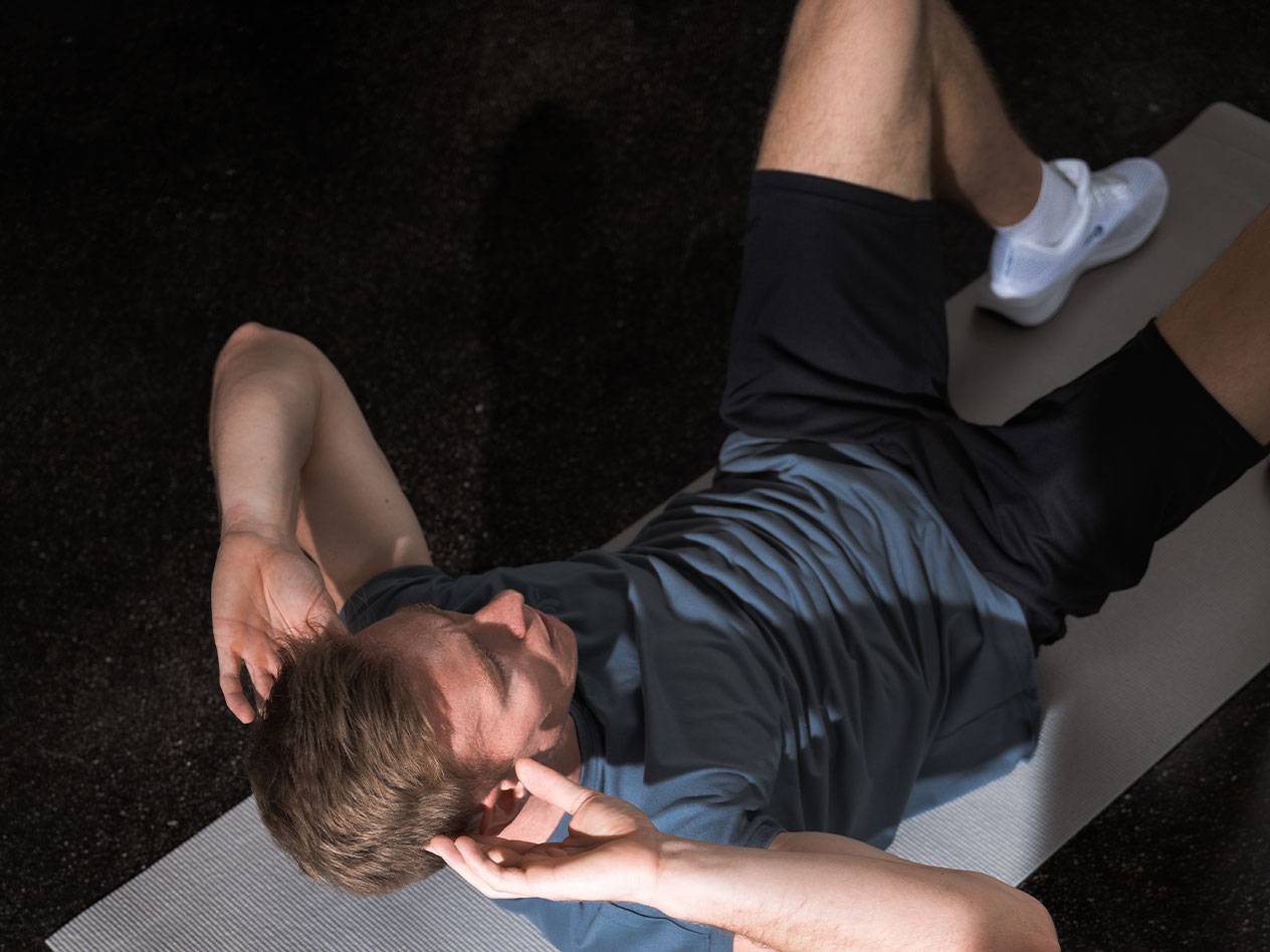 Homme en t-shirt bleu et short noir faisant des abdos sur un tapis de yoga.