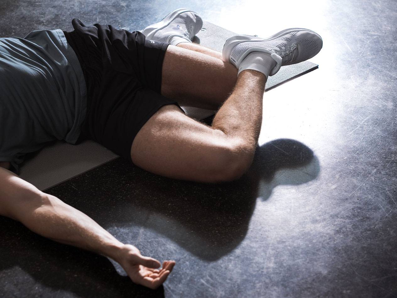 Homme allongé sur un tapis de sport en tenue et chaussures de sport.