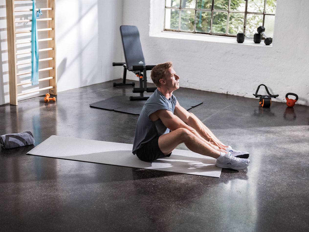 Un homme s'étire sur un tapis de yoga dans une salle de sport avec équipement.