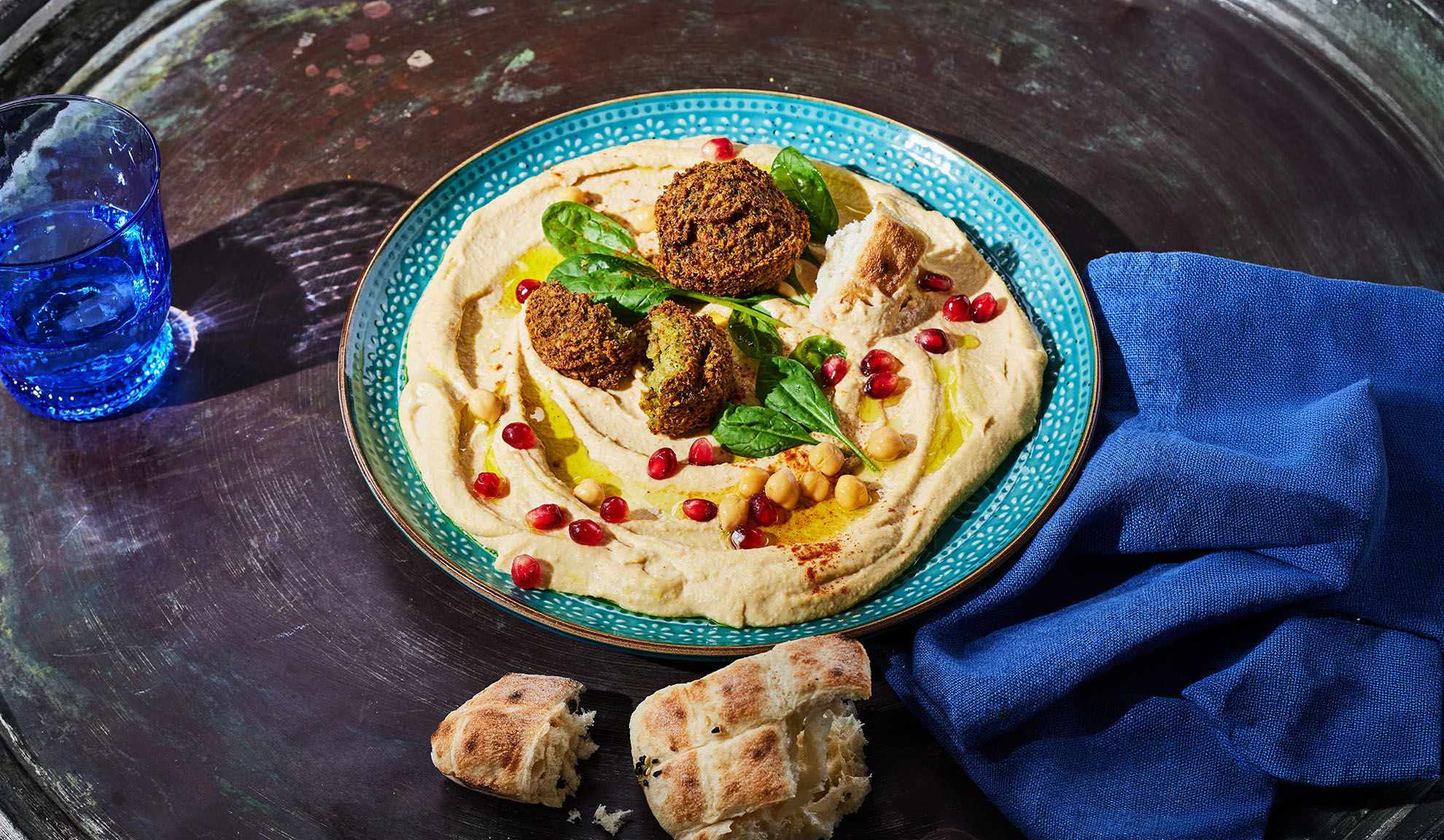 Houmous avec falafels, graines de grenade et pain pita sur une table sombre.