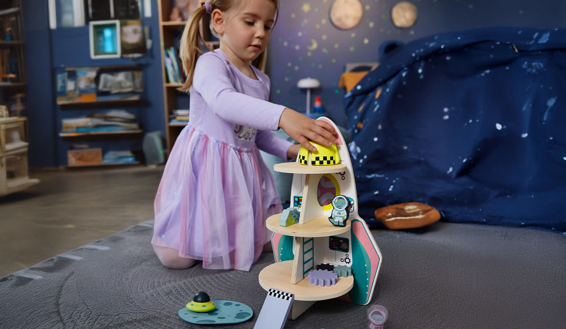 Una bambina gioca con un razzo giocattolo e accessori spaziali in una stanza a tema.