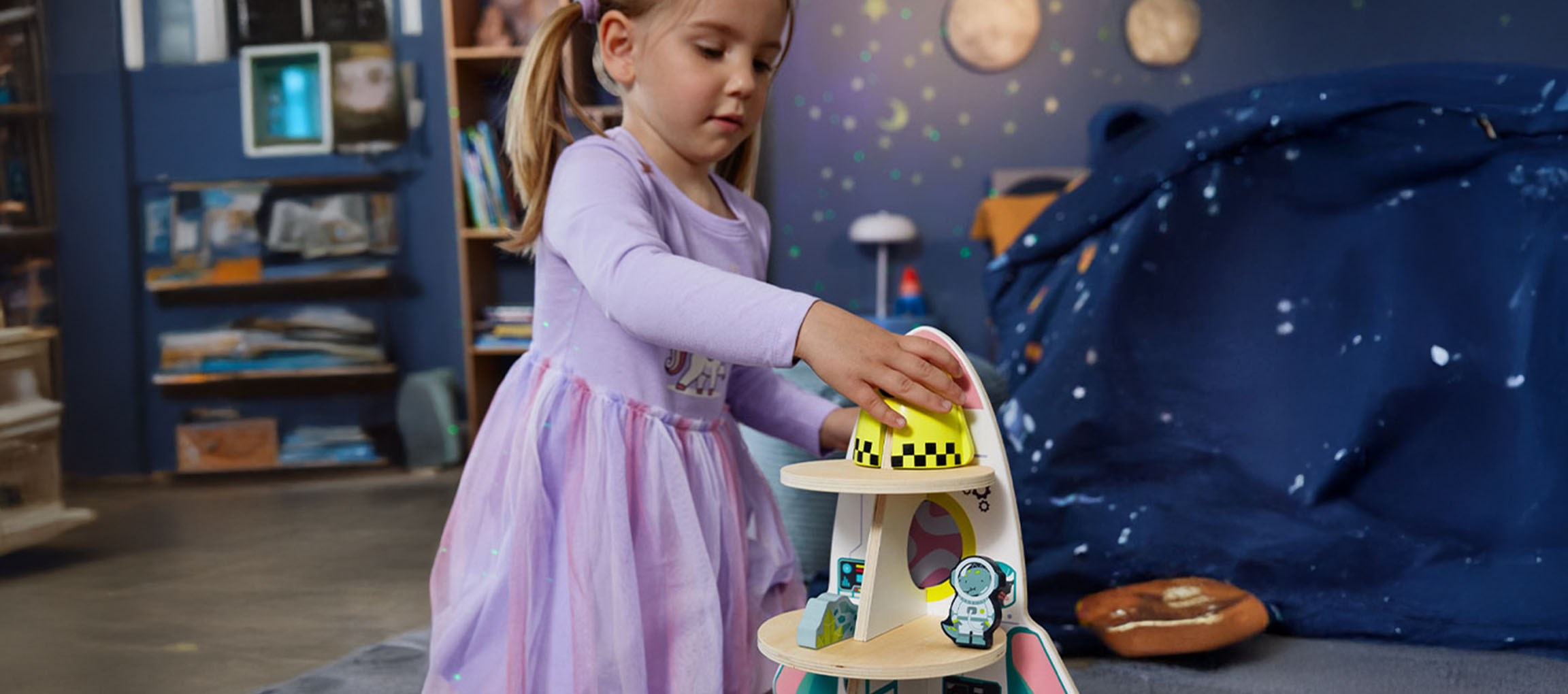 Bambina che gioca con un giocattolo a forma di astronave in una stanza a tema spaziale.