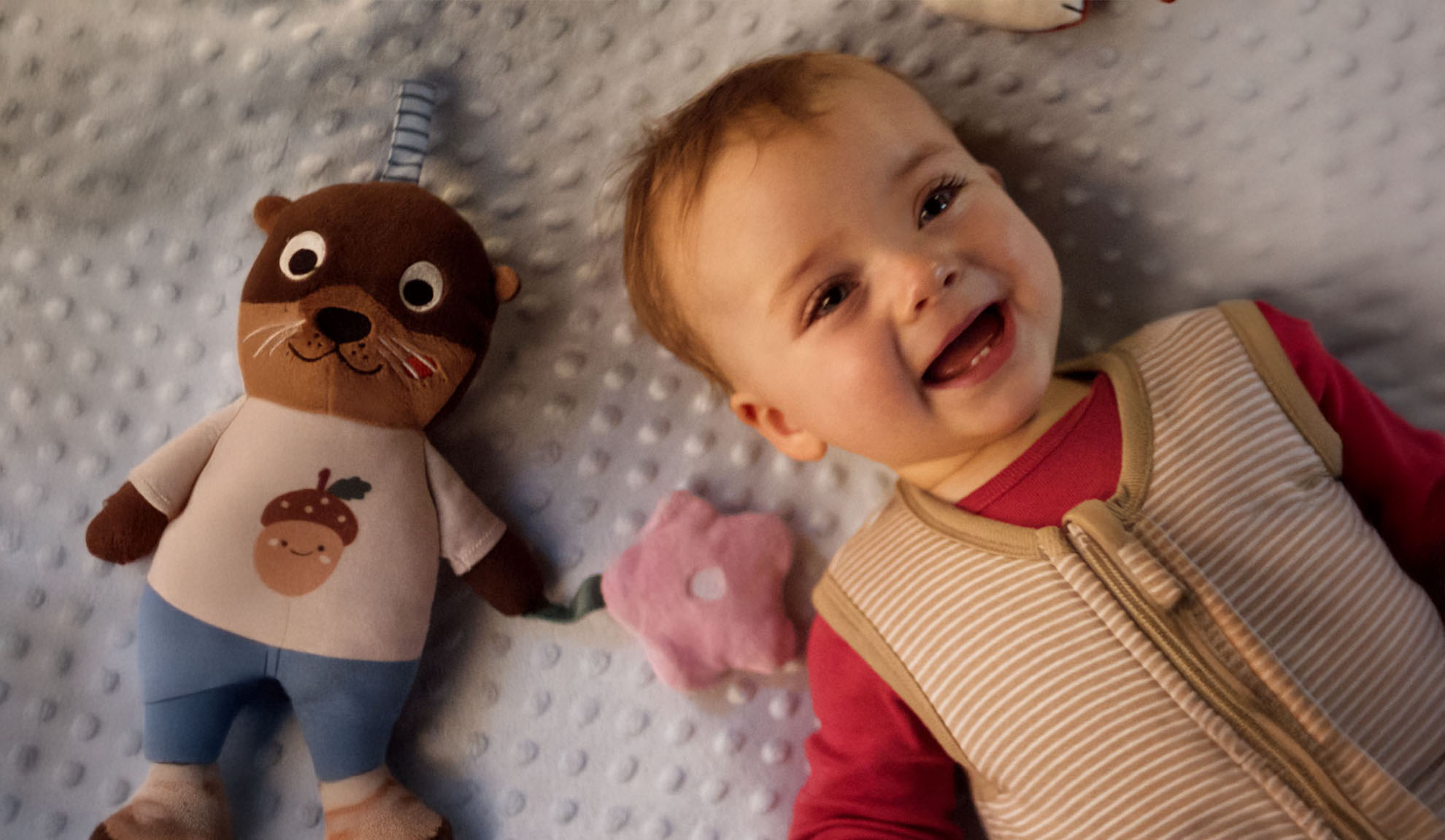 Un bambino sorridente e un peluche di lontra su una coperta morbida.