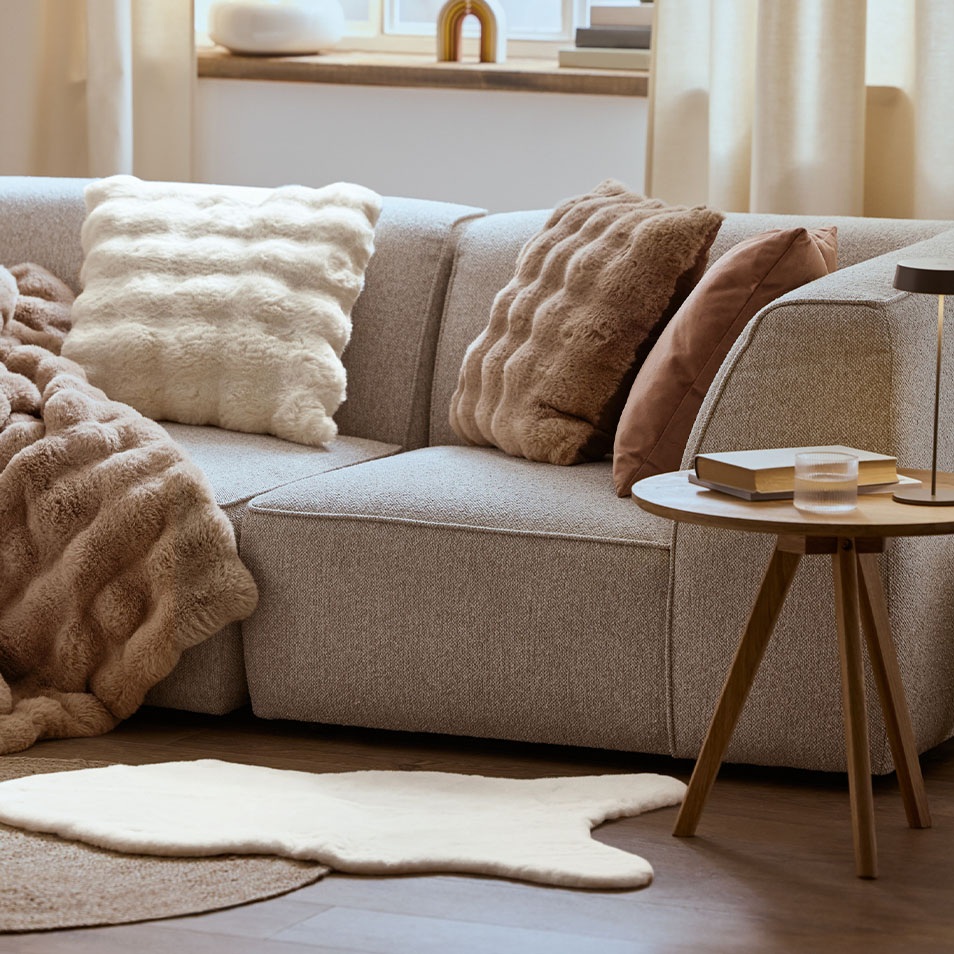 Un divano modulare grigio con cuscini e una coperta soffici, accanto a un tavolino in legno.