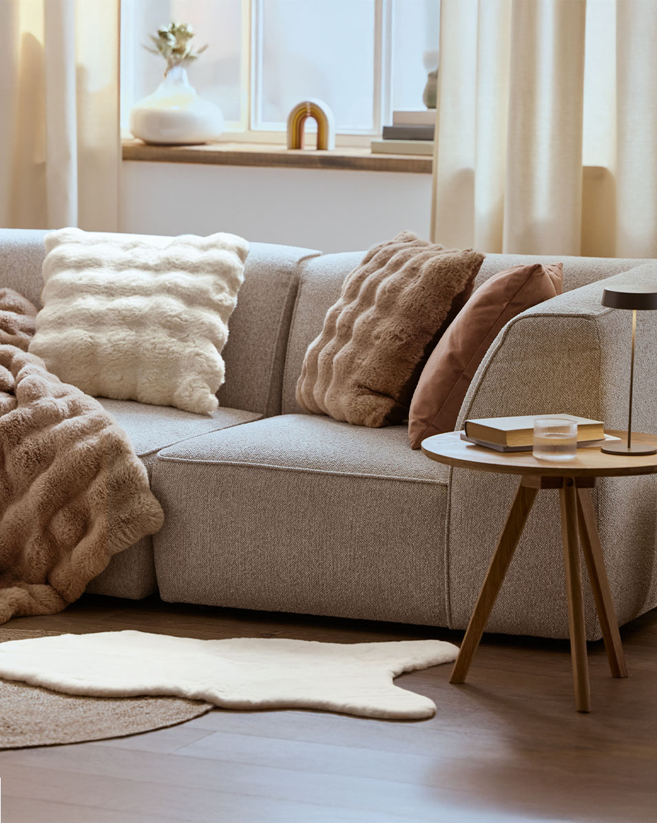 Divano modulare grigio con cuscini e coperte soffici, tavolino laterale in legno.