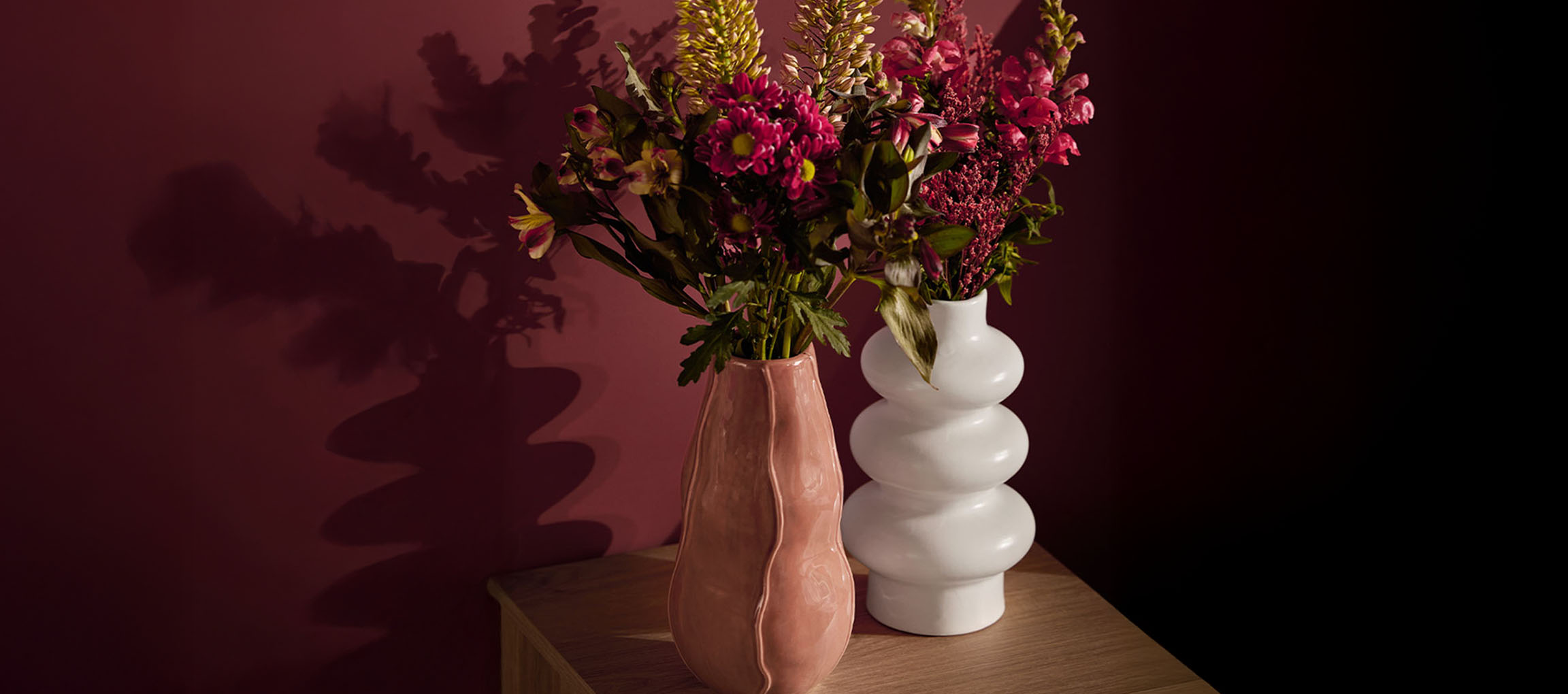 Due vasi con fiori, uno rosa e uno bianco, su una superficie di legno.