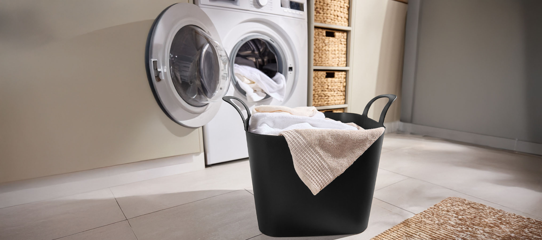 Lave-linge avec porte ouverte et panier à linge rempli de linge propre dans une buanderie.
