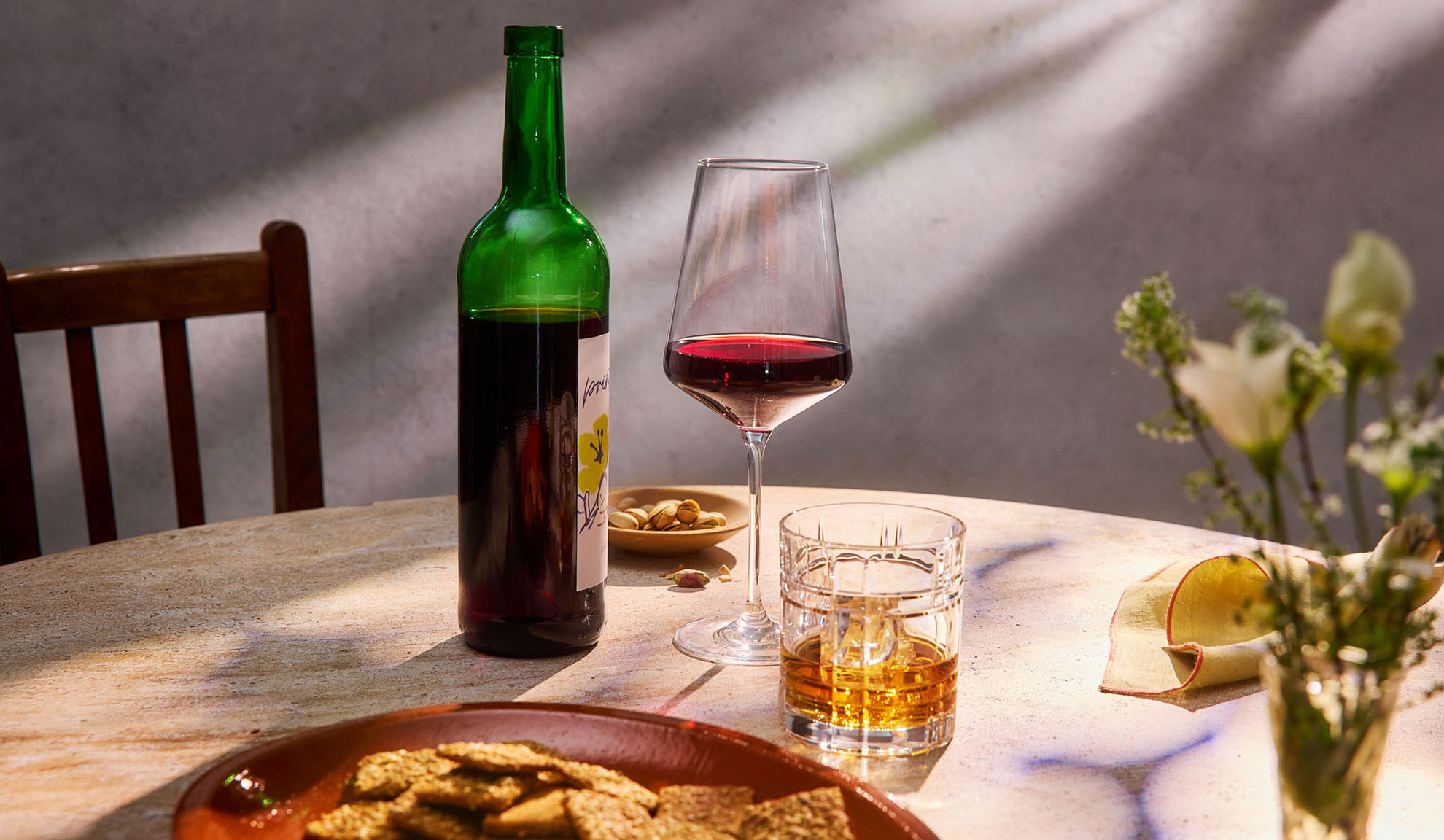 Rotwein, Whisky und Snacks auf einem Tisch im Sonnenlicht.