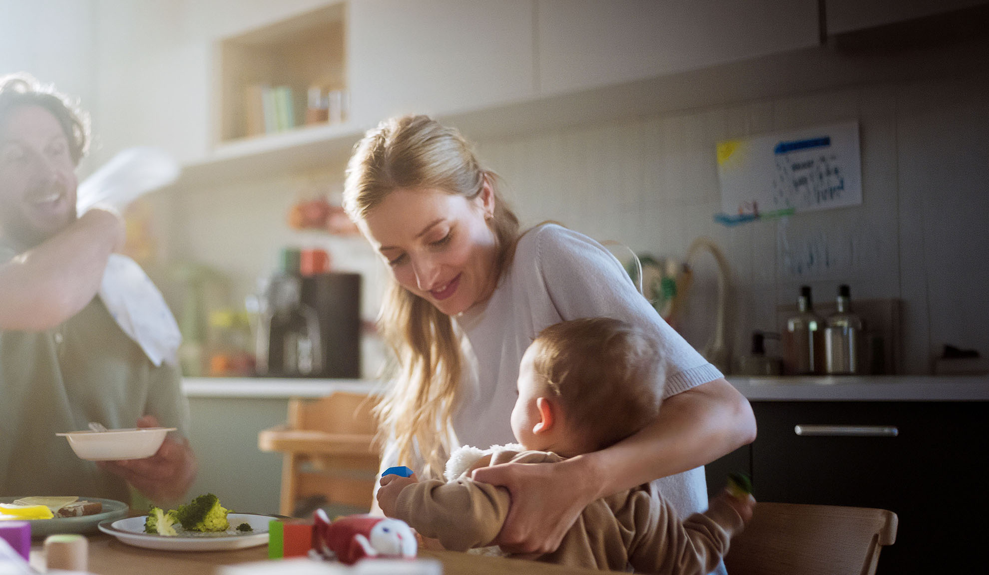 Famiglia che mangia insieme in cucina, la madre aiuta il bambino a mangiare.