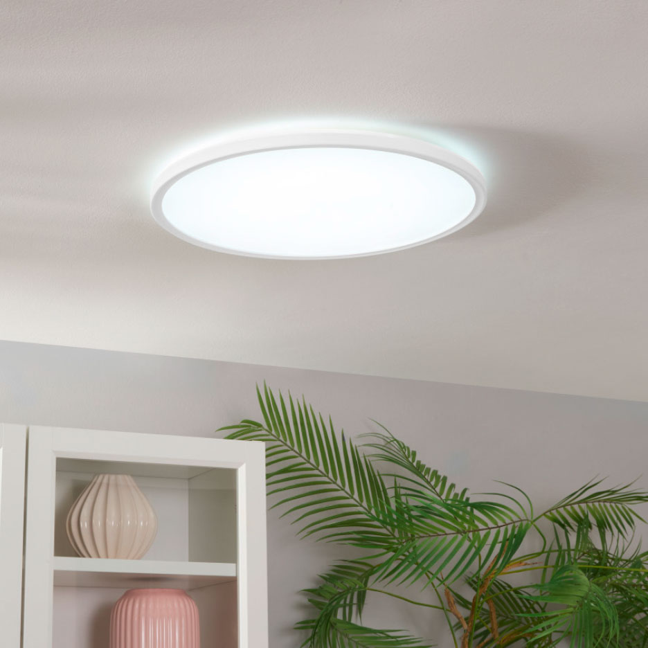 Runde weiße LED-Deckenleuchte an einer hellen Decke, mit einem Schrank und einer Pflanze unten.
