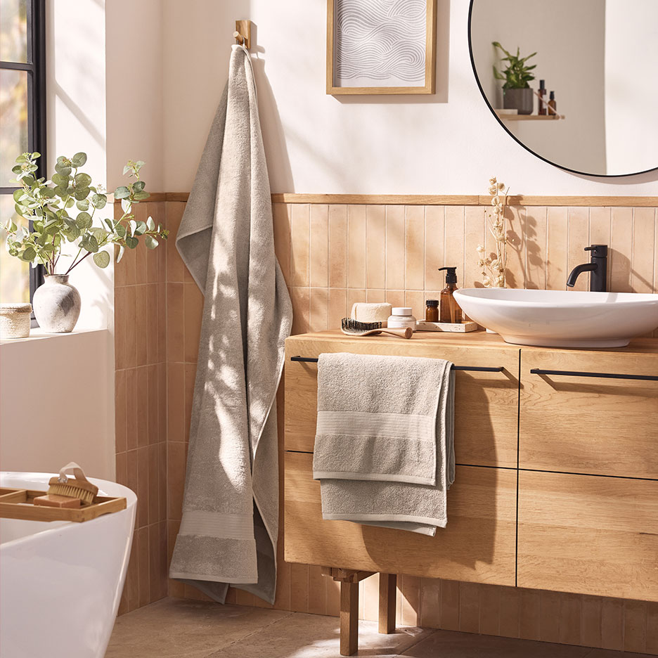 Modernes Badezimmer mit beigen Handtüchern, weißem Waschbecken und Holzmöbeln.