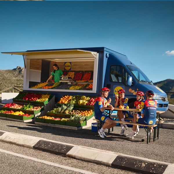 Ciclisti si riposano vicino a un camion Lidl pieno di frutta e verdura.