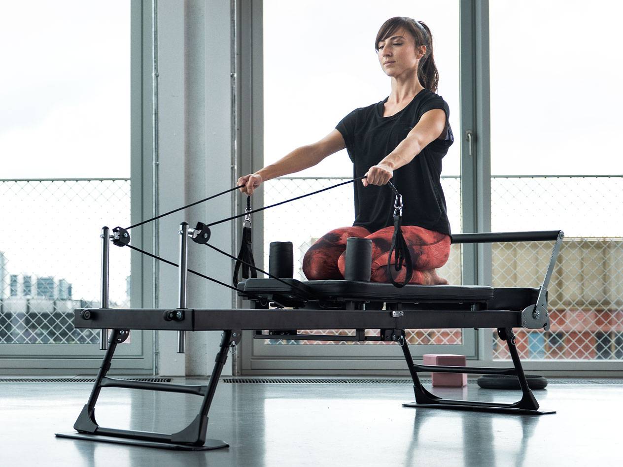 Donna che fa Pilates su un reformer con grandi finestre sullo sfondo.