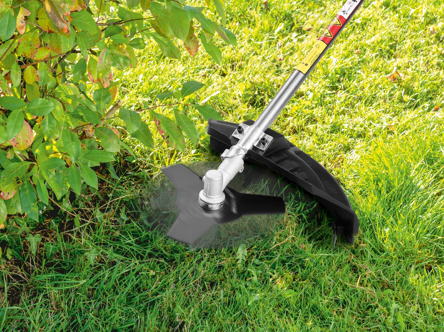 Decespugliatore con lama metallica che taglia l'erba vicino a un cespuglio.