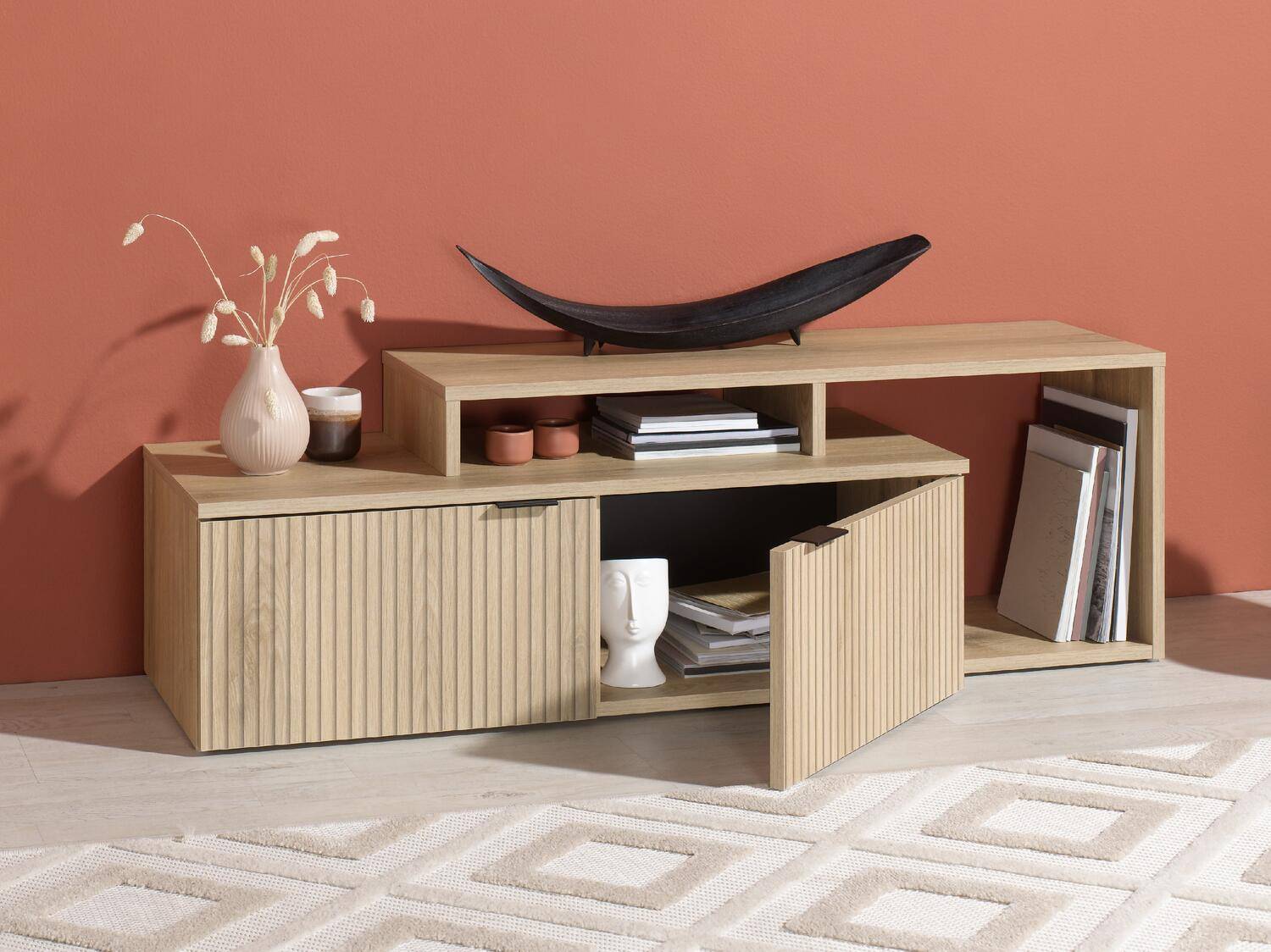 Heller Holz-TV-Schrank mit geriffelten Türen, dekoriert mit Vasen und Büchern.