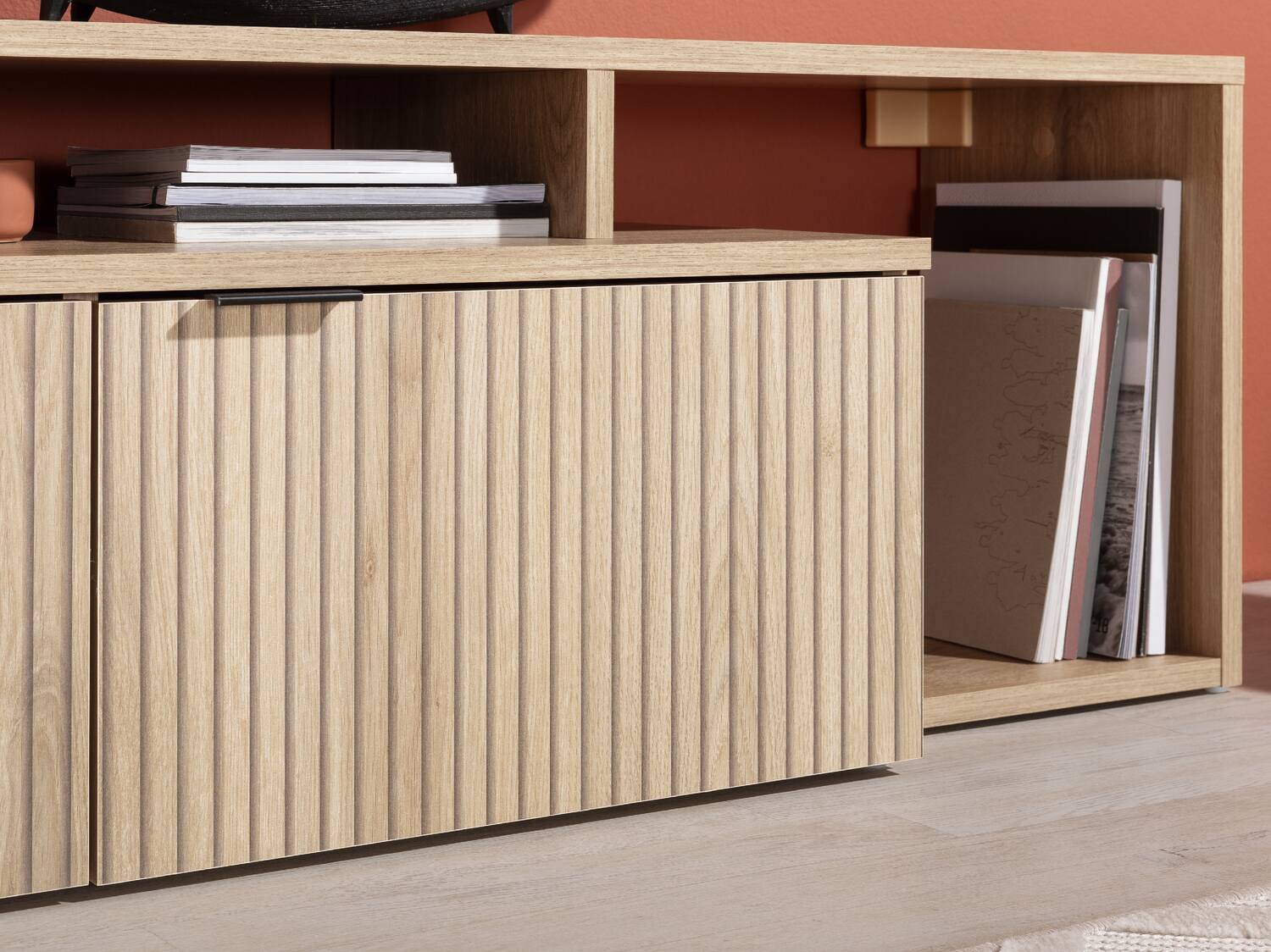 Helles Holz-TV-Möbel mit geriffelten Türen und offenen Regalen mit Büchern.