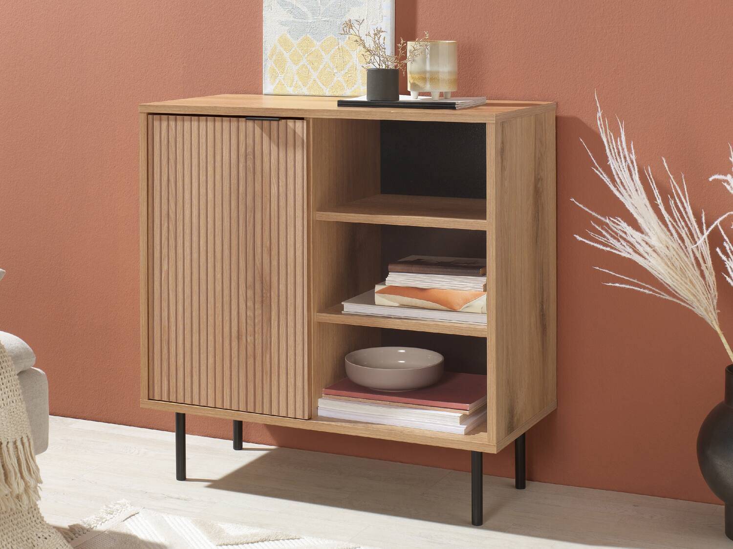 Heller Holzschrank mit Rollladentür und offenen Regalen, auf schwarzen Beinen.
