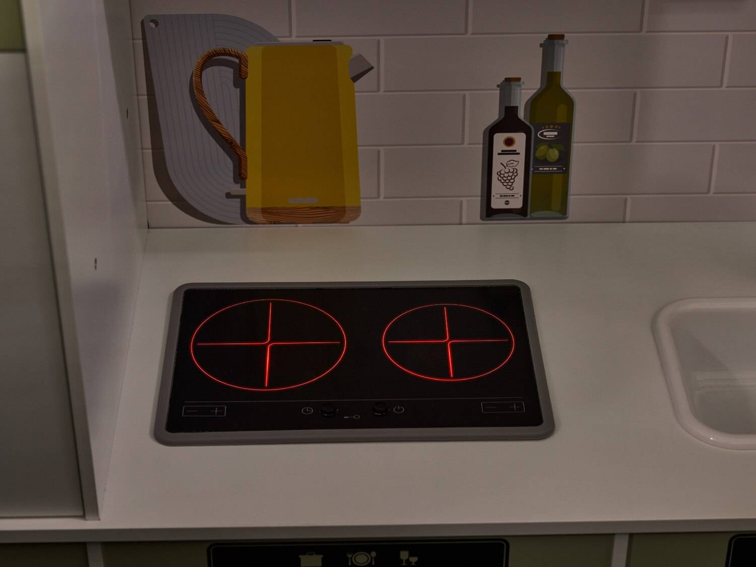Cucina giocattolo con piani cottura illuminati, bollitore giallo e bottiglie decorative.