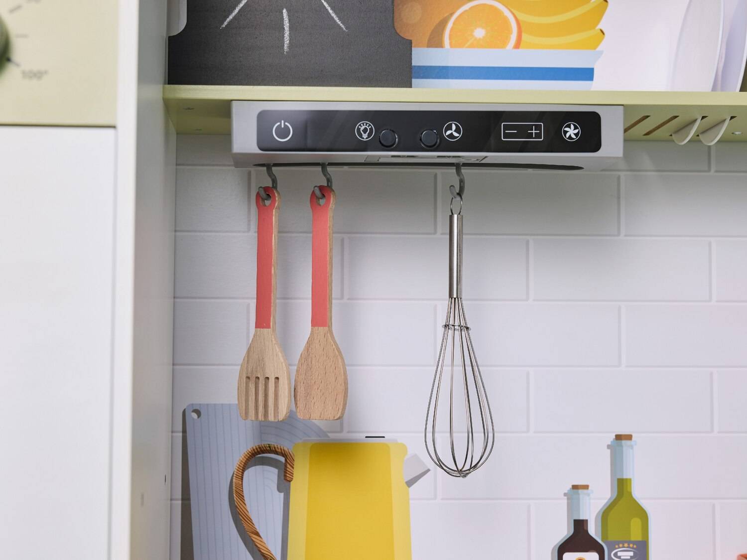 Utensili da cucina in legno e frusta appesi sotto una cappa giocattolo.
