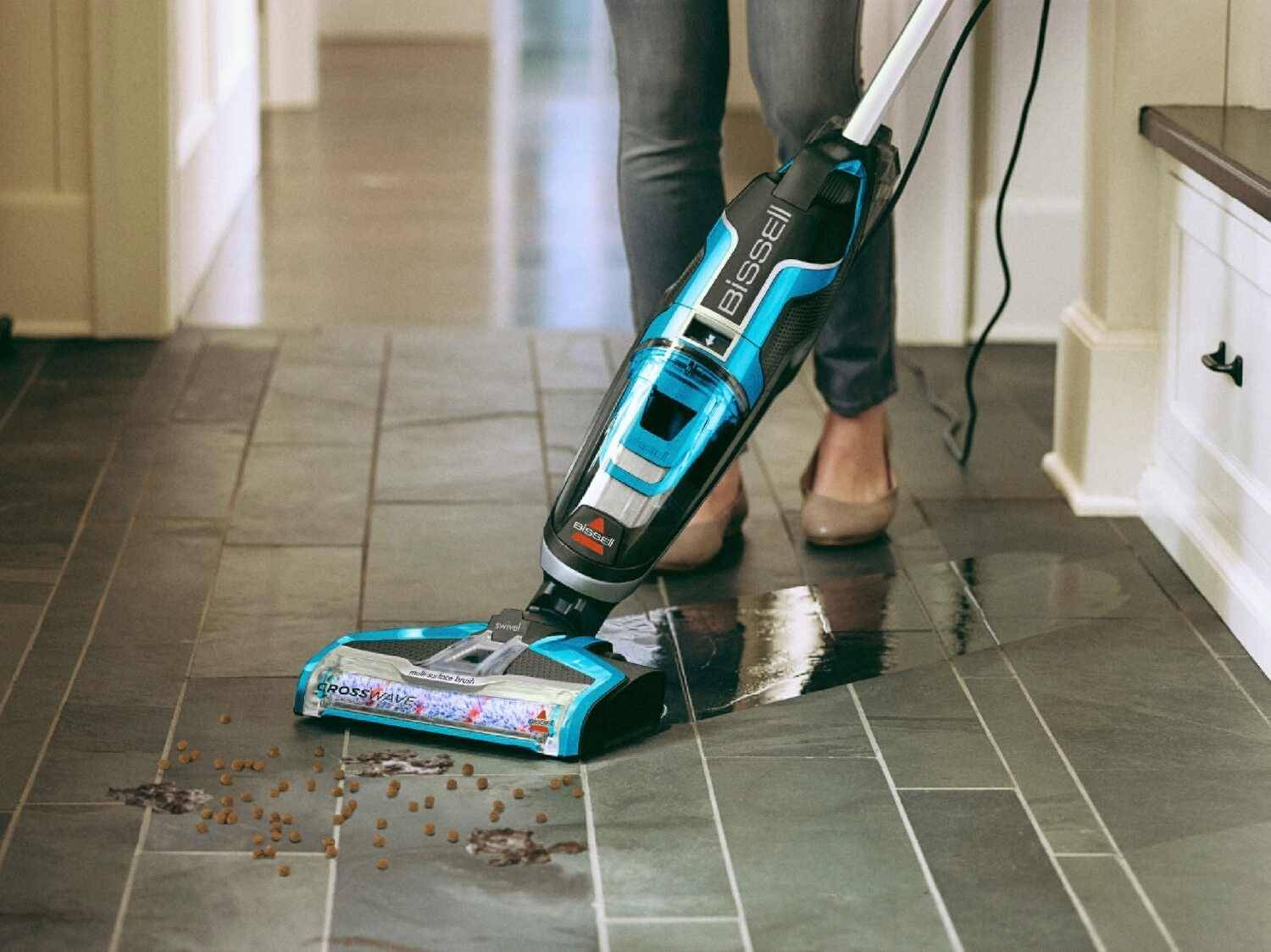 Ein Bissell CrossWave Bodenreiniger säubert Flecken und Trockenfutter auf dunklen Fliesen.