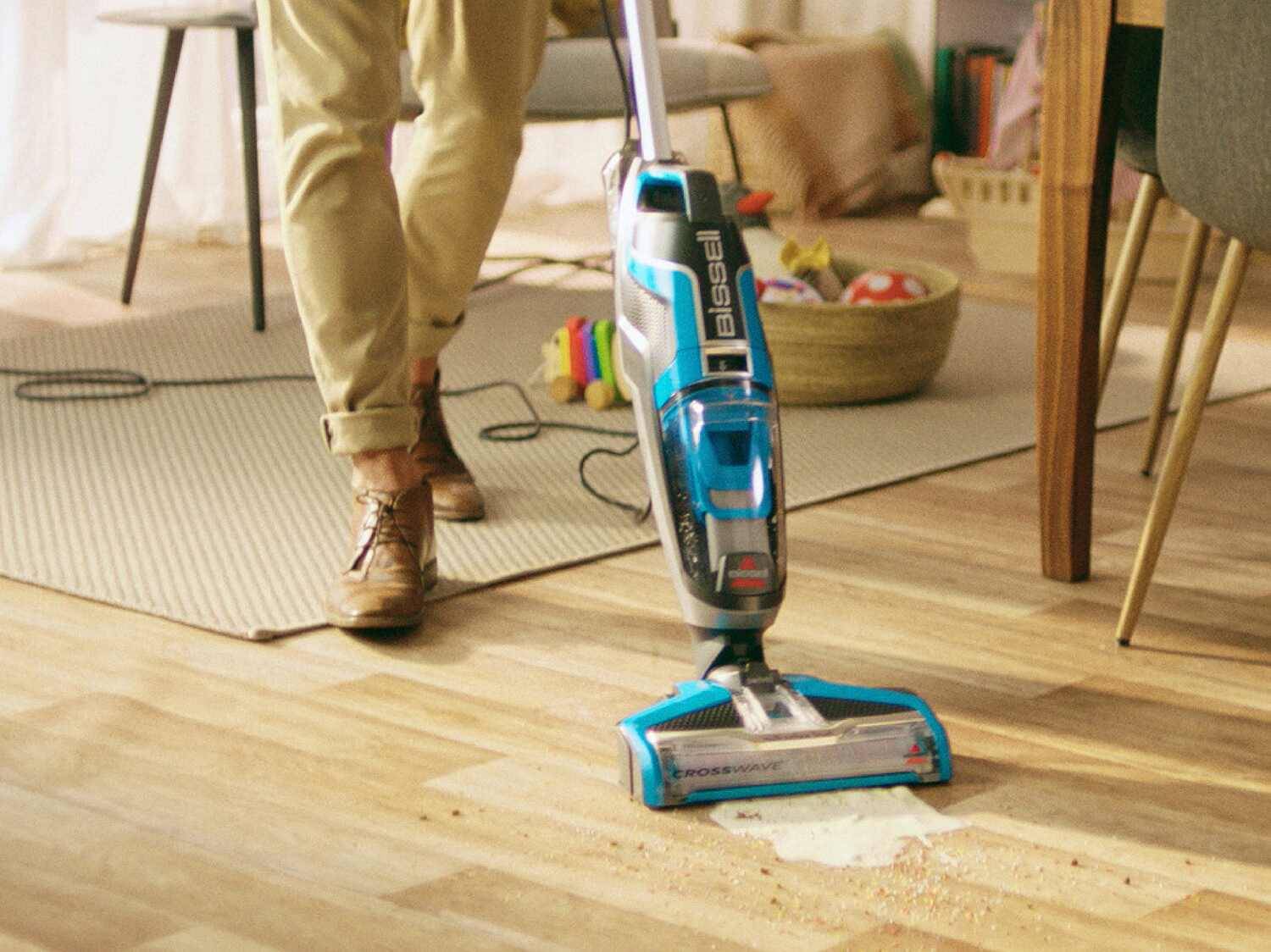 Ein Bissell CrossWave Staubsauger reinigt einen Holzboden mit einer Person im Hintergrund.