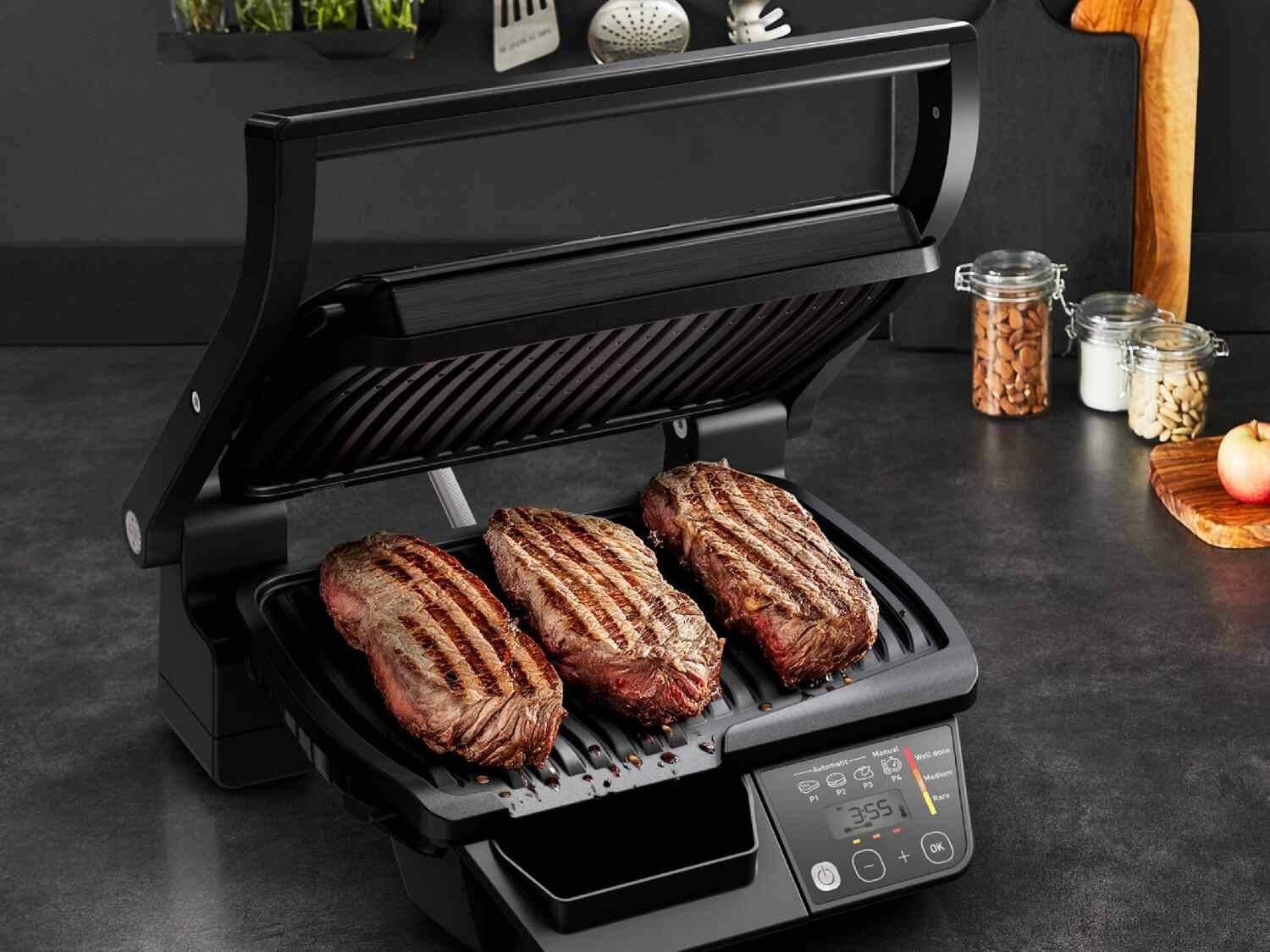 Elektrischer Grill mit drei gegrillten Steaks, 3:55 auf dem Display.