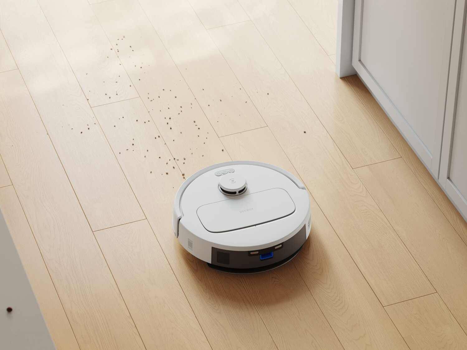 Weißer Saugroboter auf hellem Holzboden mit verstreutem Schmutz.