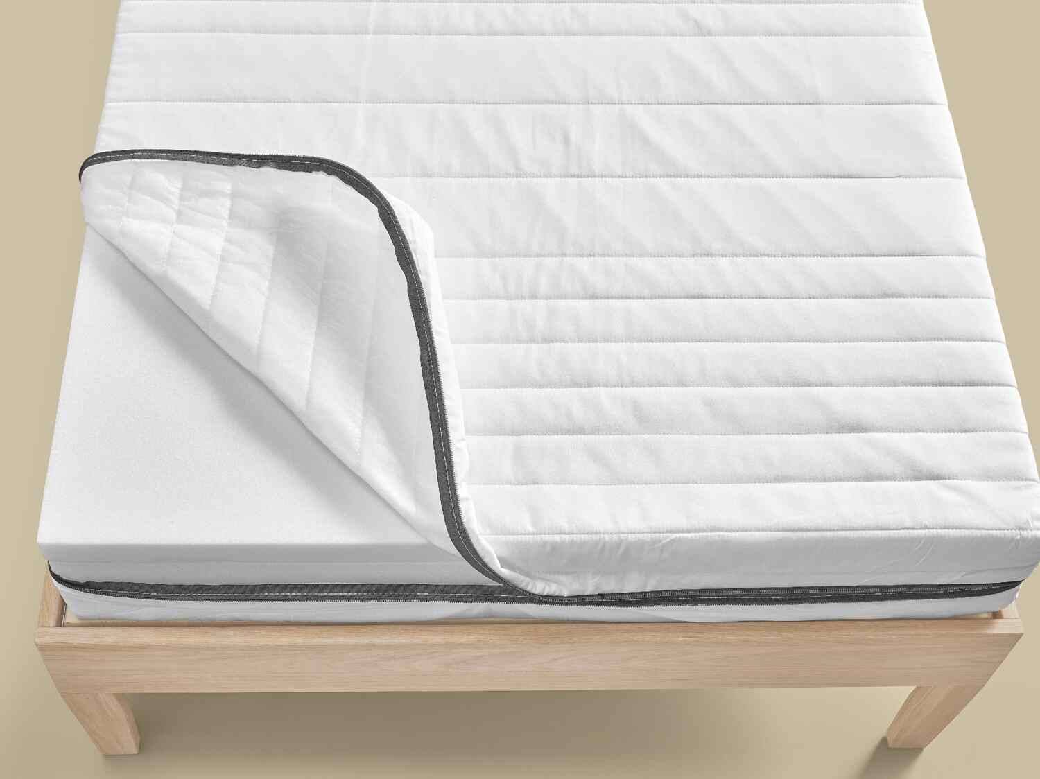 Weiße Matratze mit teilweise geöffnetem, gestepptem Bezug auf einem Holzlattenrost.