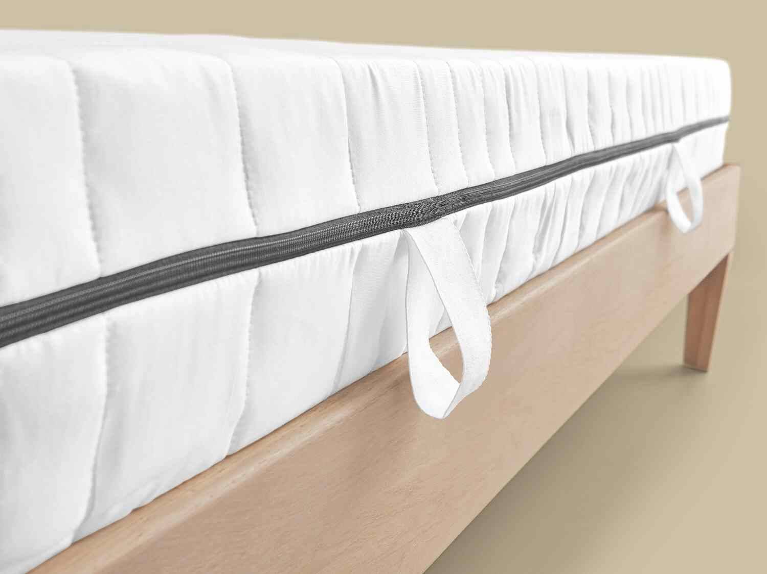 Weiße Matratze mit grauem Reißverschluss und Griffen auf einem hellen Holzlattenrost.