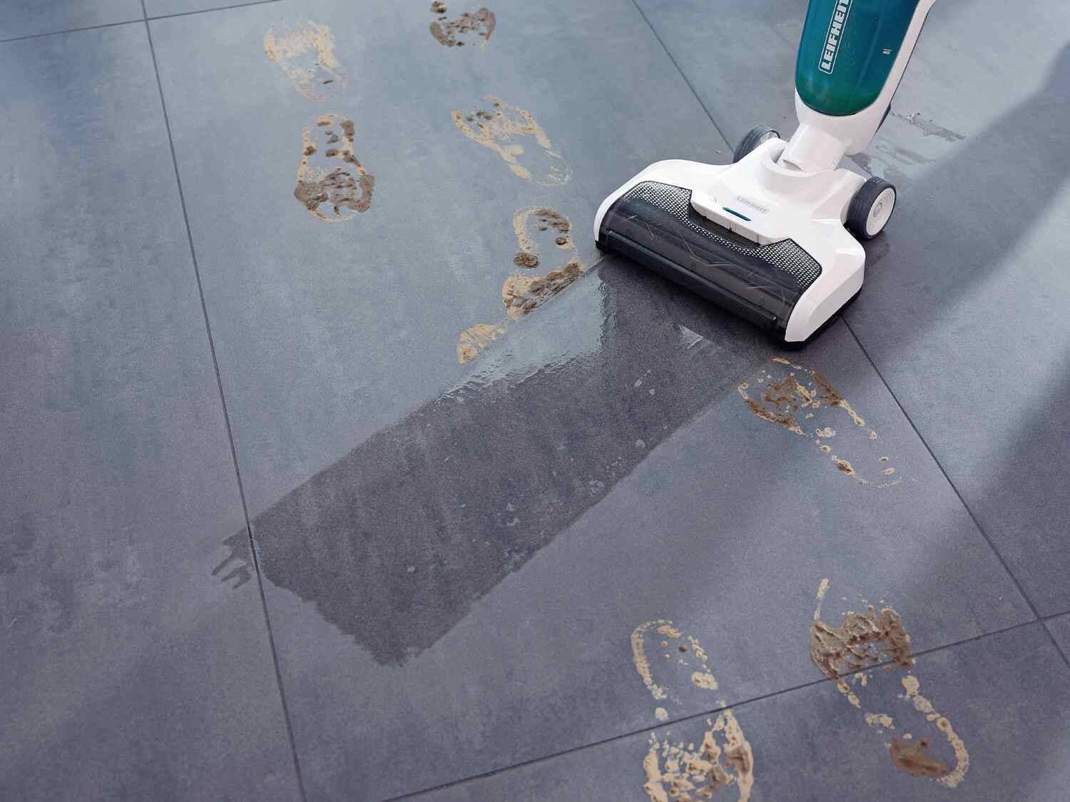 Ein Leifheit Bodenreiniger säubert schlammige Fußabdrücke auf grauen Fliesen.