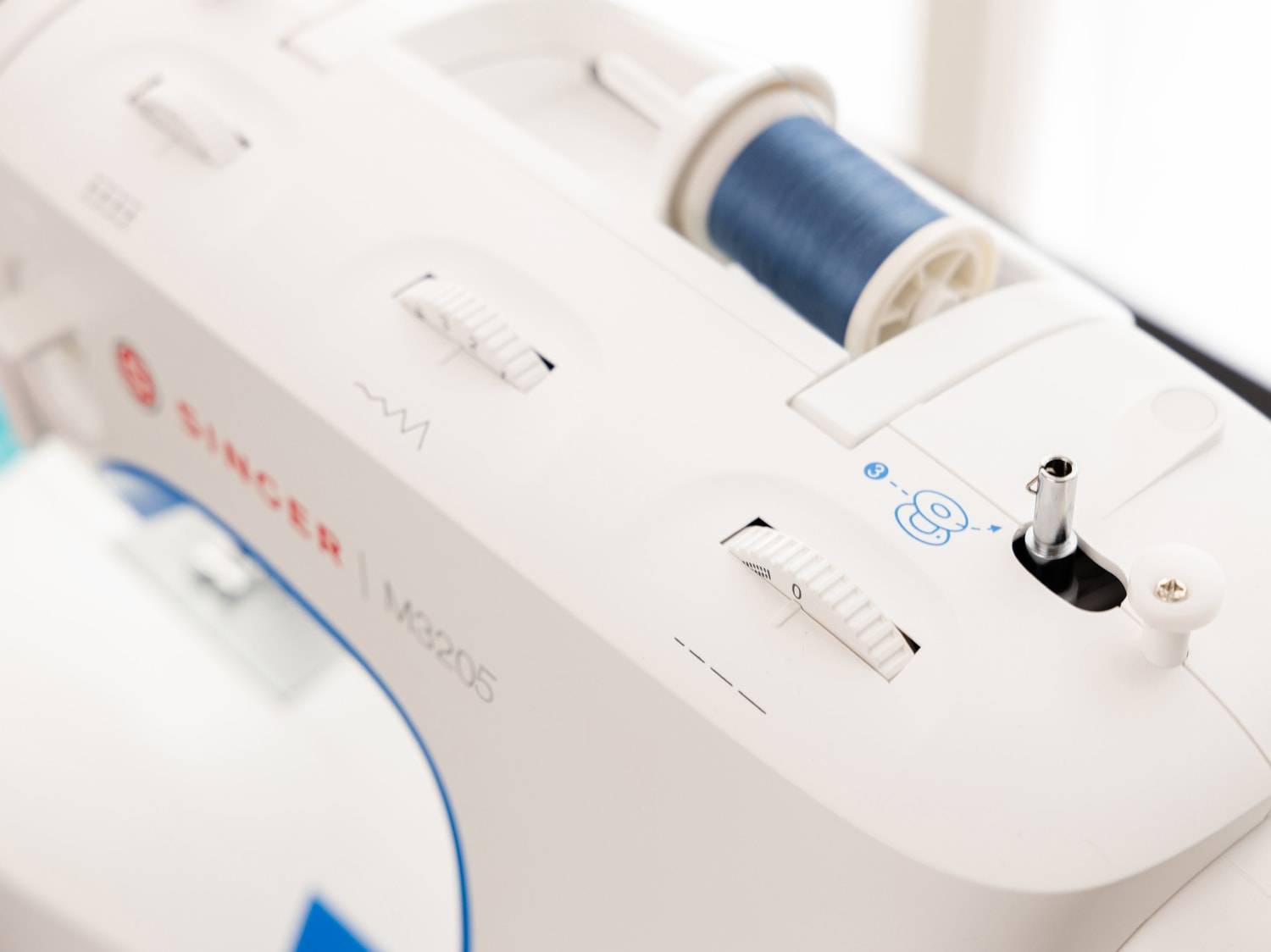 Gros plan d'une machine à coudre blanche avec une bobine de fil bleu et des boutons de réglage.