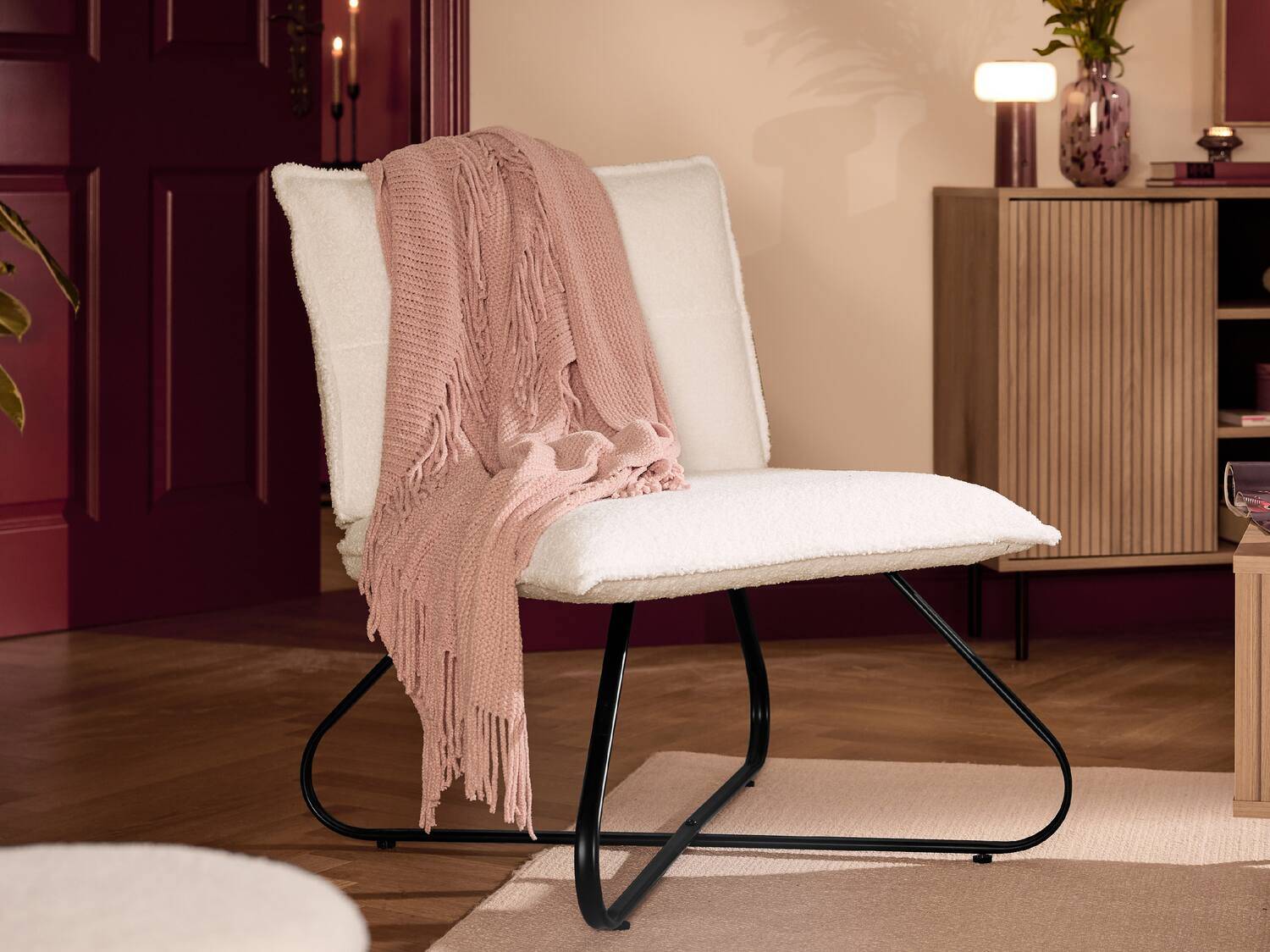 Weißer Sessel mit rosa Decke in einem gemütlichen Wohnzimmer.