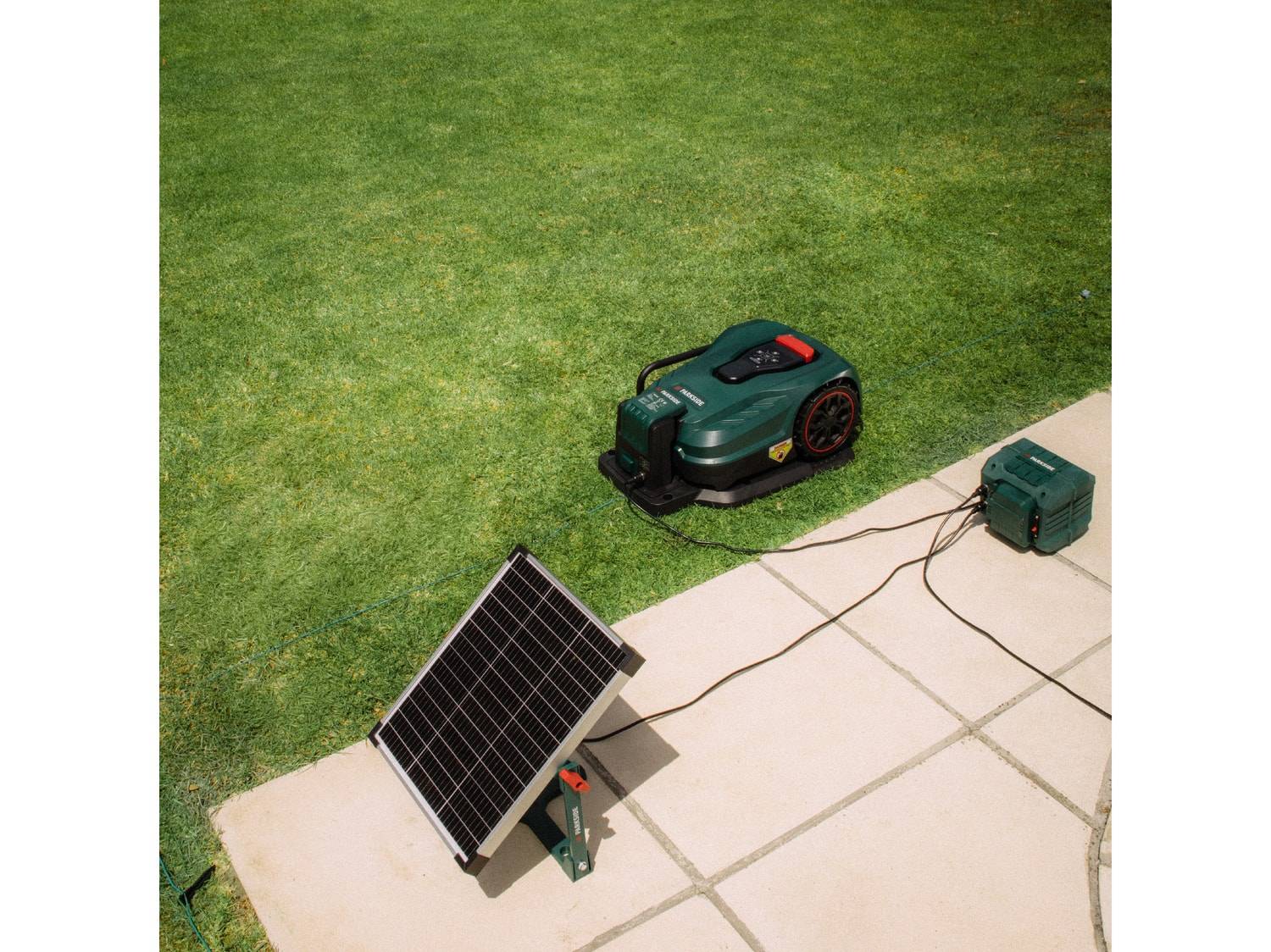 Robot tondeuse vert avec station de charge et panneau solaire sur pelouse et terrasse.