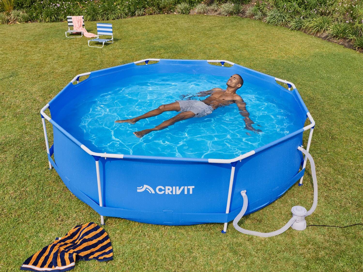 Un homme se détend dans une piscine hors sol bleue dans le jardin, avec des serviettes à côté.