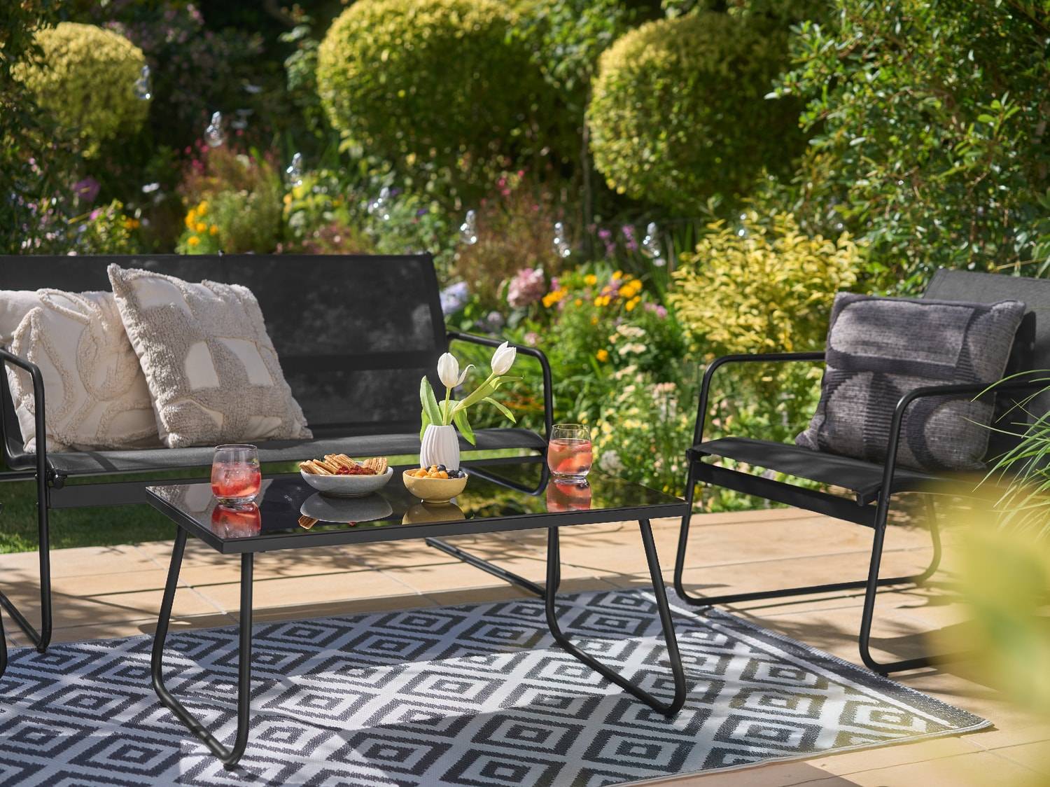Salon de jardin noir avec table basse, canapé et fauteuil, sur un tapis géométrique.