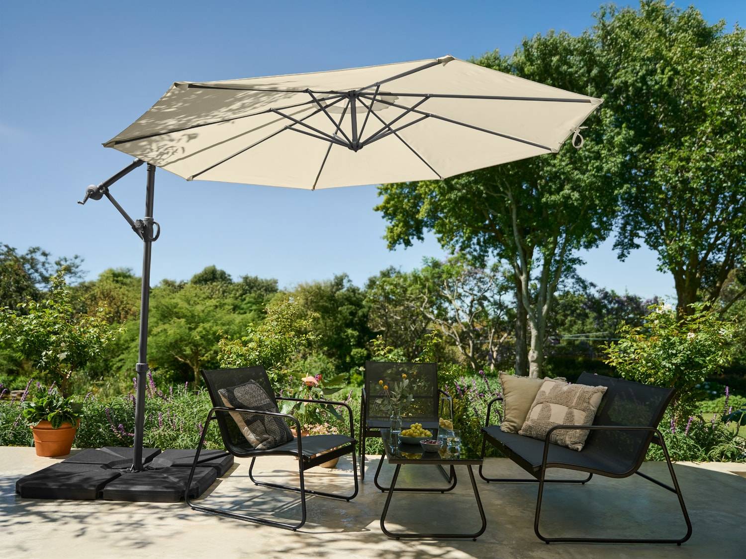 Salon de jardin avec parasol déporté, deux fauteuils et une table basse.