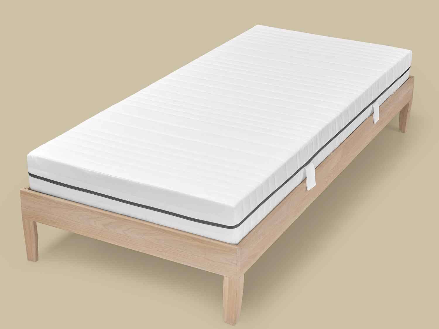 Weiße gestreifte Matratze auf einem hellen Holzlattenrost.