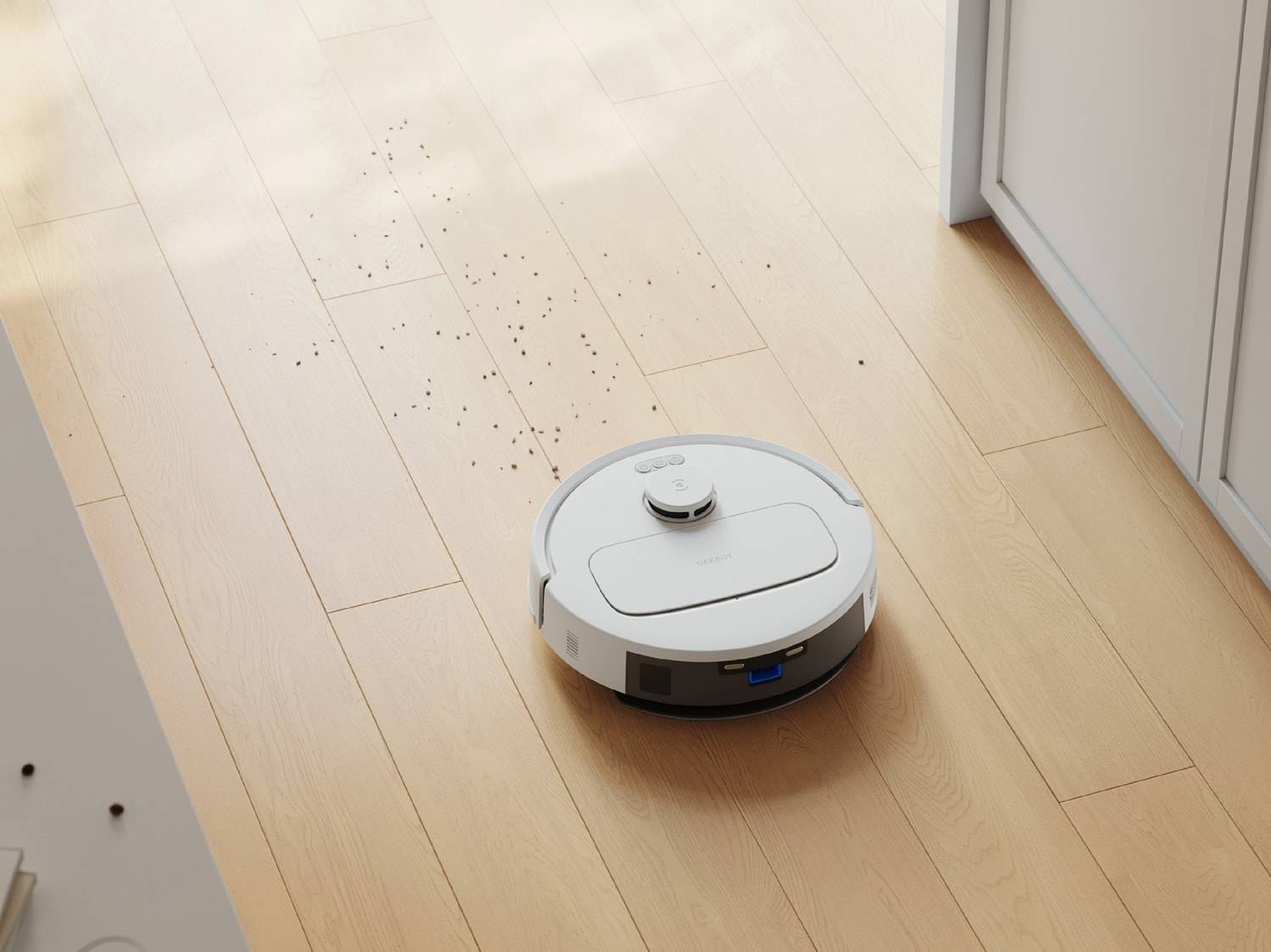 Un robot aspirateur blanc sur un parquet clair avec des saletés.
