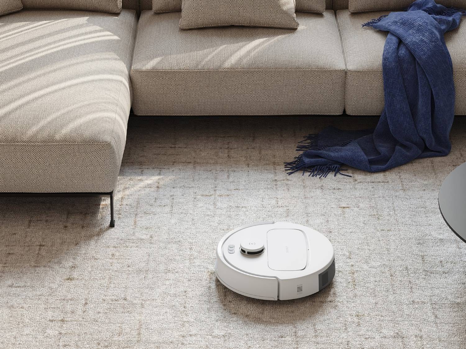 Robot aspirateur sur tapis devant un canapé avec une couverture bleue