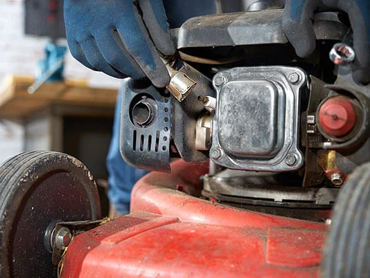 Mani guantate che sostituiscono la candela di un tosaerba rosso.