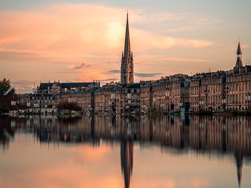 Paesaggio urbano di Bordeaux al tramonto con una chiesa e il suo riflesso nell'acqua.